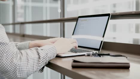 Young-Asian-business-man-using-laptop-computer-in-working-space-with-smartphone-and-notebook-on-wooden-desk.-Male-hand-typing-on-laptop-keyboard.-Freelance-lifestyle-in-digital-age-concept.