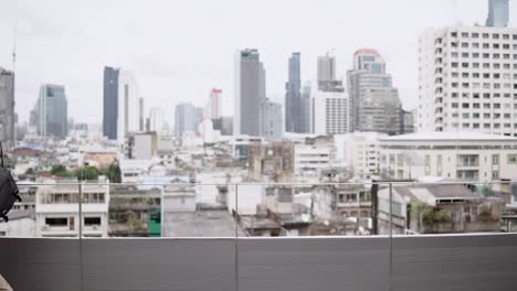 Young-Asian-businessman-using-smartphone-for-business-talk-walking-on-office-building-rooftop-terrace-with-city-view-in-the-background.-Business-communication-and-corporation-concepts.