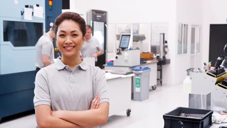 Portrait-Of-Female-Engineer-On-Factory-Floor-Of-Busy-Workshop