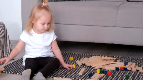 Little-charming-blond-girl-playing-wood-blocks-sitting-near-the-sofa.
