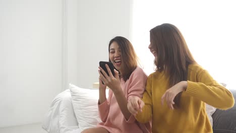 Gerne-asiatische-Lesben-Lgbt-paar-genießen-Sie-Unterhaltung-im-Wohnzimmer.-Schöne-Frauen-auf-einem-Sofa-liegend,-hören-Sie-Musik-auf-Smartphone-zu-Hause.