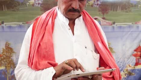 Handheld-Indian-man-busy-on-a-touchscreen-tablet-with-a-wonderfully-colourful-tent-backdrop