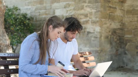 einige-junge-Studenten-Mann-und-Frau-gemeinsam-mit-Laptop-Computer-in-einer-Straße-im-Freien-im-Sommer