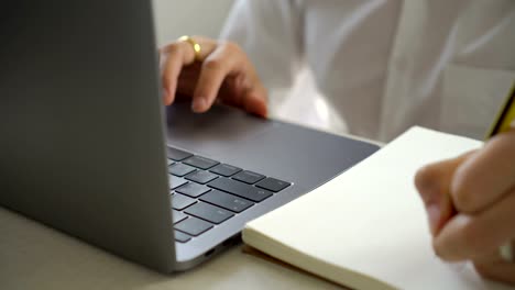 Close-up-businessman-using-laptop-and-writing-notes-on-notebook.