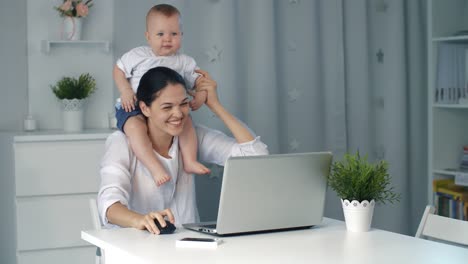 Madre-con-bebé-trabajando-en-ordenador-portátil-en-casa