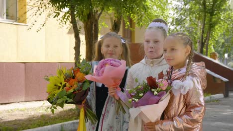 Fröhliche-Schulmädchen-mit-Blumen-sprechen-und-in-der-Nähe-von-Schule-zusammenstehen