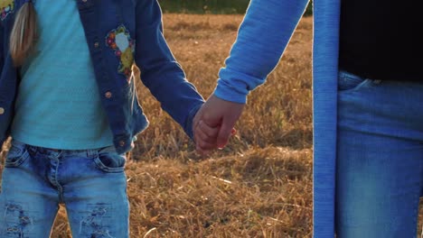 Mom-holding-dancing-daughter-by-hand-on-wheat-field-background.