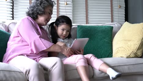 Ältere-Frau-und-Kinder-sitzen-zusammen-im-Wohnzimmer-zu-Hause-mit-Tablet-PC.-Konzept-der-Familie,-Bildungstechnologie,-wachsende-lernen,-psychische-Gesundheit-und-Entwicklung-des-Alters.-4-k-Auflösung.