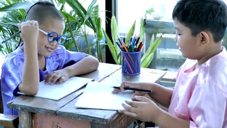 Happy-little-asian-boy-with-writing-in-notebook-and-pencils-drawing-at-home.-education-concept