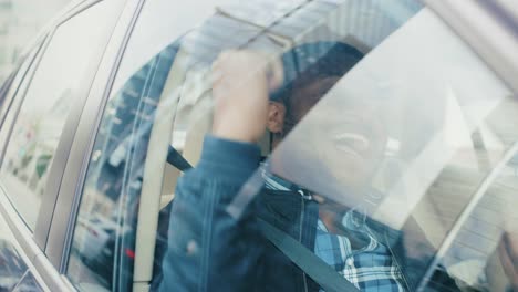 Hübscher-erfolgreichen-schwarzen-Mann-reitet-auf-dem-Beifahrersitz-eines-Autos,-er-freut-sich-und-tanzt.-Blick-auf-die-große-Stadt-spiegelt-sich-im-Fenster.-Kamera-Auto-außen-bewegen.