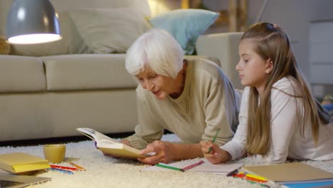 Liebevolle-Oma-macht-Hausaufgaben-mit-Mädchen-auf-dem-Boden