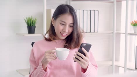 Mujer-asiática-de-negocios-inteligente-hermosa-en-ropa-casual-elegante-con-smartphone-y-beber-una-taza-caliente-de-café-sentado-en-la-mesa-de-la-oficina-creativa.-Mujeres-de-estilo-de-vida-trabajando-en-el-concepto-de-oficina.