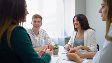 one-guy-and-three-girls-sitting-at-table-and-talking-to-each-other-in-school-library