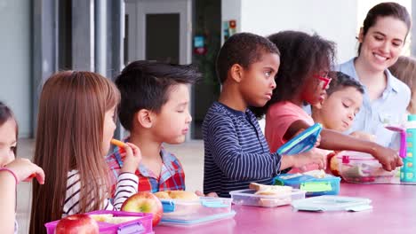 Escuela-primaria-niños-comiendo-en-la-mesa-con-comidas