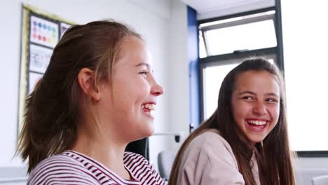 Dos-estudiantes-de-secundaria-de-la-mujer-riéndose-mientras-se-sientan-en-el-aula