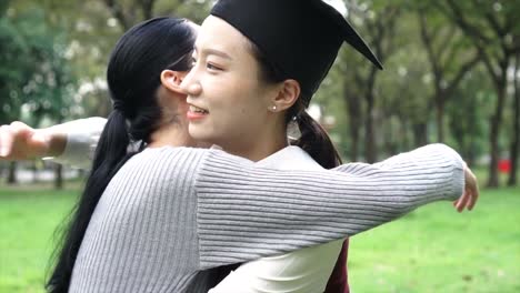 Young-Asian-female-graduate-hugging-her-friend-at-graduation-ceremony-in-slow-motion.-International-diversity-background