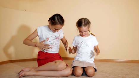 Hermanitas-sentado-en-el-piso-y-pintura-de-una-camiseta-con-las-manos