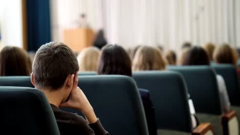 Rückansicht-des-gelangweilt-Zuhörer-im-Saal-sitzen-und-hören-mit-dem-Lautsprecher