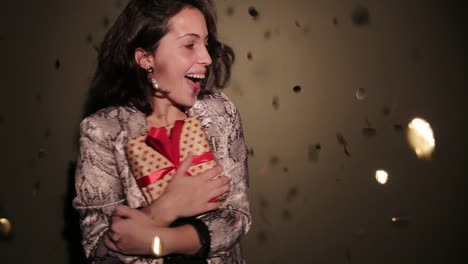 Brunette-happy-woman-hold-her-present,-spin-with-confetti-in-pink-background-wear-red-dress