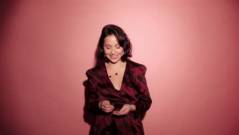 Brunette-happy-woman-throw-up-and-laugh-to-camera-with-confetti-in-pink-background-wear-red-dress