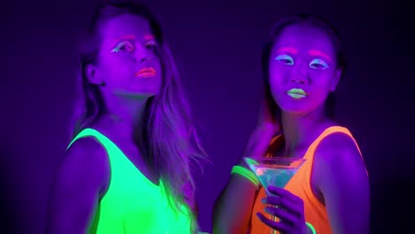 Langsame-Motin-von-schönen-sexy-Frauen-mit-fluoreszierenden-Make-up-und-Kleidung-Tanz-im-Neonlicht.-Night-Club,-Party-Konzept.