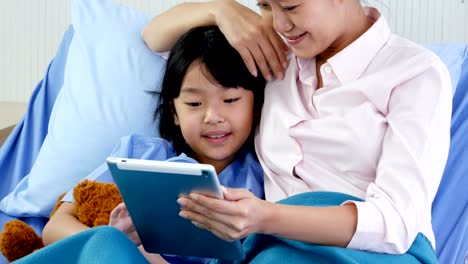 Little-girl-and-her-mom-using-tablet-together-at-hospital.-People-with-Technology,-Family,-Healthcare-and-Medical-Concept.