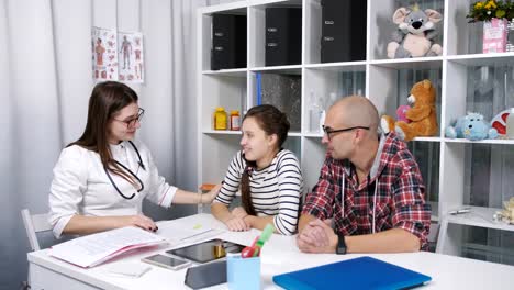 Doctor-amable-escribe-un-adolescente-después-de-su-enfermedad-y-abraza-a-su-adiós.-Padre-e-hija-adolescentes-dados-de-alta-después-de-una-enfermedad-en-la-oficina-del-doctor.