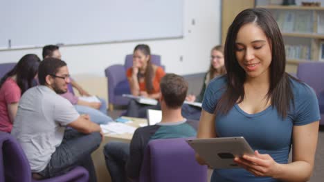 Portrait-of-a-young-woman-using-a-tablet-and-standing-in-front-of-her-classmates