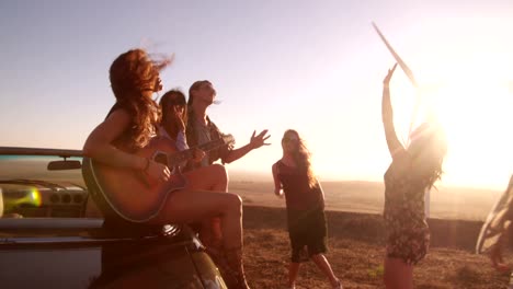 Hipster-amigos-disfrutando-de-viaje-con-una-guitarra-durante-la-puesta-del-sol