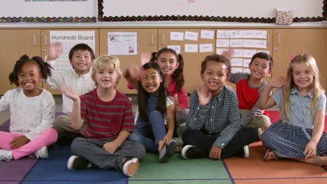 Niños-de-escuela-primaria-clase-Siéntese-saludar-con-la-mano-a-la-cámara