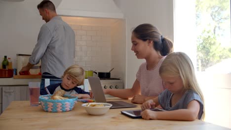 Kinder-am-Küchentisch-mit-Mama,-während-Papa-kocht