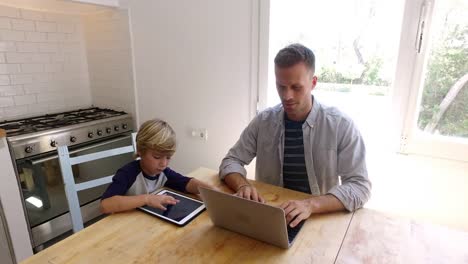 Padre-e-hijo-usando-computadoras-en-la-mesa-de-la-cocina