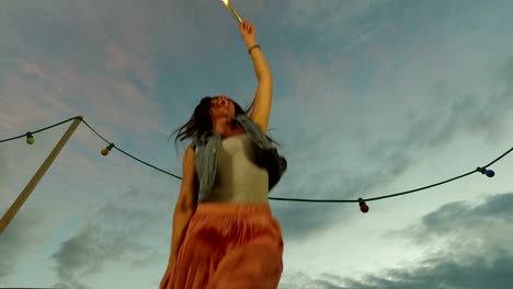 Under-view-of-brunette-woman-jumping-with-firework-candle-on-the-rooftop-terrace