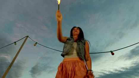 Low-angle-view-of-happy-woman-jumping-with-firework-candle