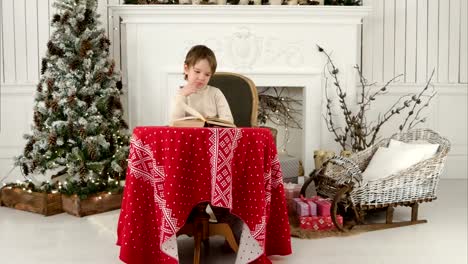 Smiling-boy-exploring-puctures-in-the-book-sitting-at-the-table-near-the-Christmas-tree