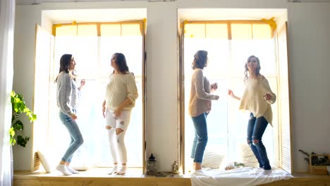 Happy-and-beautiful-girlfriends-dance-on-window-having-fun-and-joy-in-bedroom