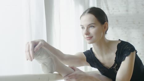 Nahaufnahme-einer-jungen-und-schönen-Ballerina-Doing-Leg-Stretching-am-Barre.-Erschossen-auf-einen-Sonnenvormittagslicht-in-einem-geräumigen-und-Light-Studio.-In-Slow-Motion.