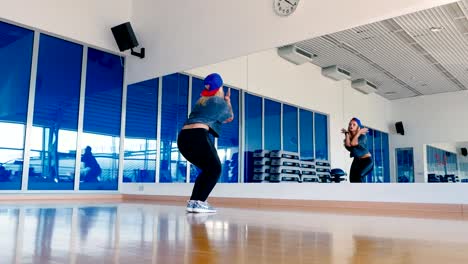 Young-girl-in-cap-dancing-hip-hop-in-front-of-the-mirror-in-gym