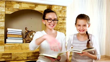 sisters-reading-textbooks-near-fireplace-at-home,-girls-smiling-and-hugging,-wearing-glasses