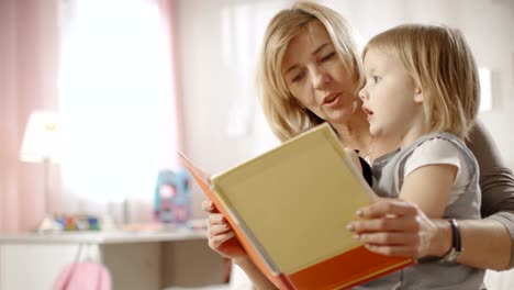 Linda-niña-se-sienta-en-el-regazo-de-su-abuela-y-leen-el-libro-de-los-niños.-Cámara-lenta.