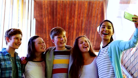 Smiling-schoolkids-taking-selfie-with-mobile-phone-in-corridor