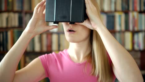 Feliz-estudiante-en-biblioteca-utilizando-gafas-de-realidad-virtual.-Estantes-de-la-librería-de-fondo