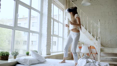 Happy-smiling-young-woman-dancing-while-getting-experience-using-360-VR-headset-glasses-of-virtual-reality-on-bed-at-home