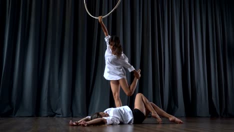 Beautiful-girl-warms-up-on-the-aerial-hoop,-her-friend-lays-on-floor