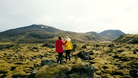 Aerial-view-of-two-woman-standing-on-the-rock-in-lava-field-in-Iceland.-Tourists-looks-on-landscape,-dancing-and-jumping