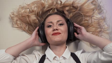 close-up-Woman-lying-on-the-bed,-listens-to-music-in-big-headphones-and-reacts-to-her-sexually-smiling