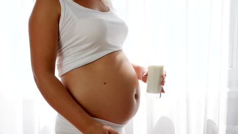 mujer-embarazada-muestra-simvol-de-aprobación-y-tiene-leche-de-cristal-sobre-fondo-de-gran-barriga,-productos-lácteos