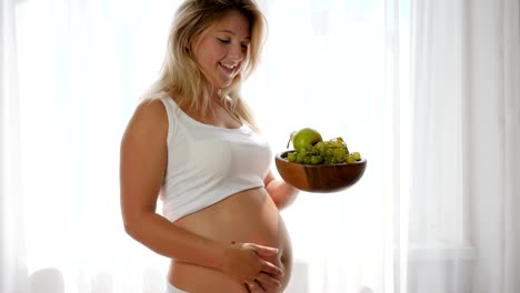 nutrition-during-pregnancy,-female-with-a-big-tummy-eats-grapes-from-a-wooden-plate