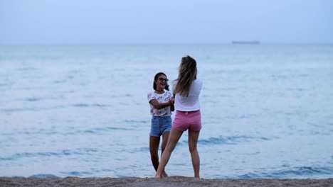 zwei-glückliche-Mädchen-Wirbeln-am-Strand-in-der-Nähe-von-das-Meer-am-Abend