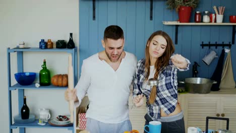 Pareja-alegre-joven-tener-diversión-bailando-y-cantando-mientras-está-la-mesa-para-el-desayuno-en-la-cocina-en-casa